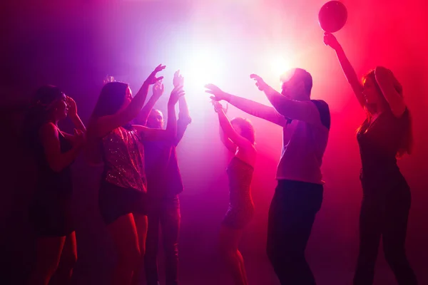 Una multitud de personas en silueta levanta las manos contra la colorida luz de neón en el fondo de la fiesta — Foto de Stock