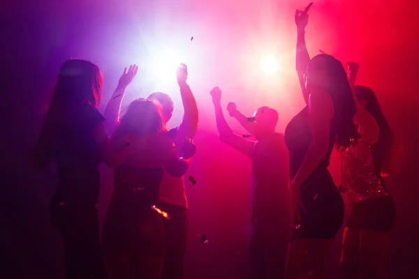 Una multitud de personas en silueta levanta las manos contra la colorida luz de neón en el fondo de la fiesta —  Fotos de Stock