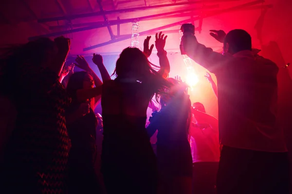 Une foule de gens en silhouette lève la main contre la lumière au néon coloré sur le fond de la fête — Photo