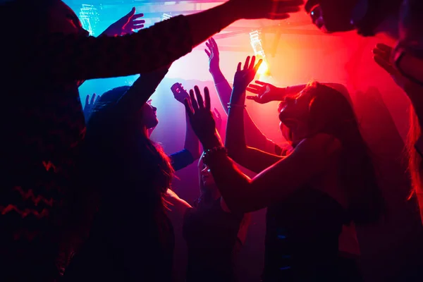 Una multitud de personas en silueta levanta las manos contra la colorida luz de neón en el fondo de la fiesta — Foto de Stock