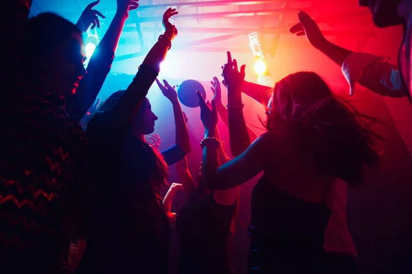 Una multitud de personas en silueta levanta las manos contra la colorida luz de neón en el fondo de la fiesta — Foto de Stock