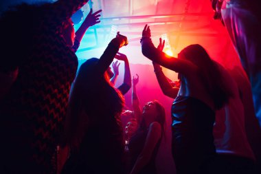 Silüetli bir kalabalık parti arka planındaki renkli neon ışığa karşı ellerini kaldırıyor.