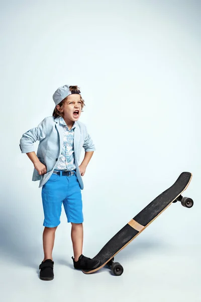 Joli jeune garçon sur skateboard en vêtements décontractés sur fond de studio blanc — Photo