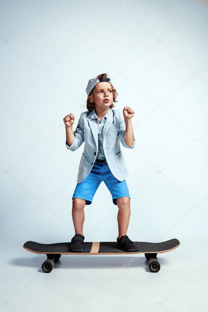 Pretty young boy on skateboard in casual clothes on white studio background