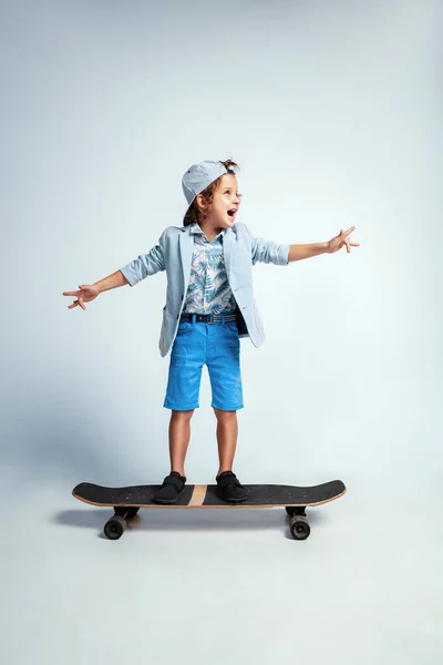 Красивый мальчик на скейтборде в повседневной одежде на белом фоне студии — стоковое фото