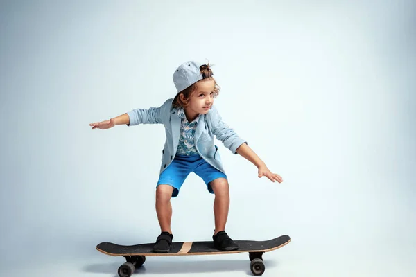 Muito jovem no skate em roupas casuais no fundo do estúdio branco — Fotografia de Stock