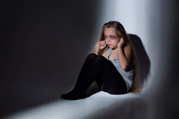 Sad and frightened little girl with bloodshot and bruised eyes sitting scared — Stock Photo, Image