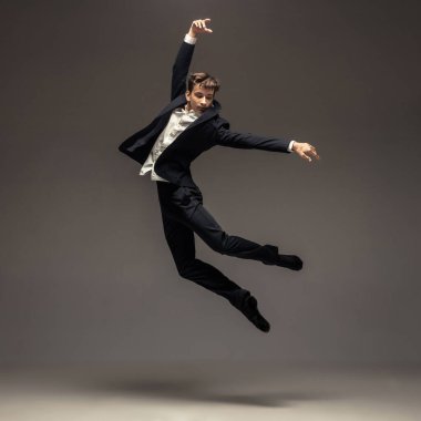 Günlük ofis tarzı giyinmiş bir adam stüdyo arka planında tek başına zıplıyor.