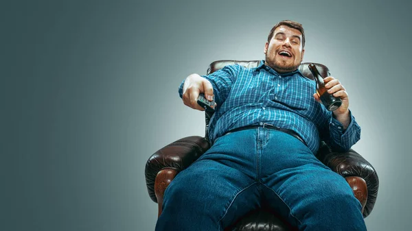 Fat man sitting in a brown armchair, emotional watching TV — ストック写真