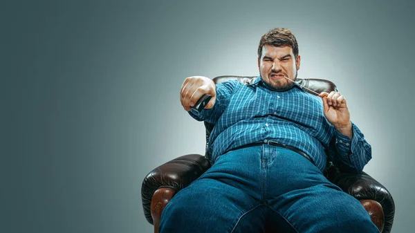 갈색 안락의자에 앉아 감성적으로 TV 를 보는 뚱뚱 한 남자 — 스톡 사진