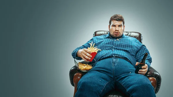 Fet man som sitter i en brun fåtölj, känslomässigt tittar på TV — Stockfoto