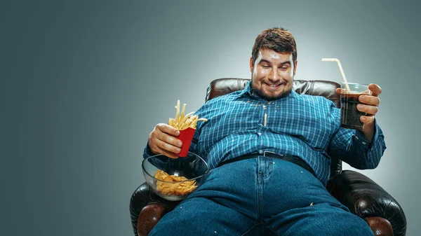 Fat man sitting in a brown armchair, emotional watching TV