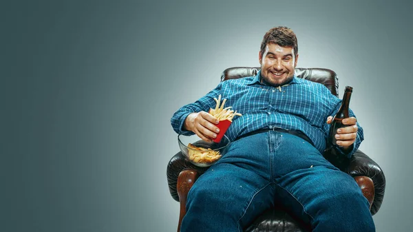 Fat man sitting in a brown armchair, emotional watching TV