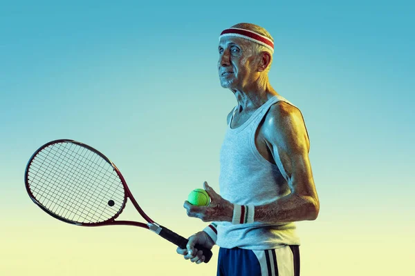 Старший мужчина играет в теннис в спортивной форме на градиентном фоне и неоновом свете — стоковое фото