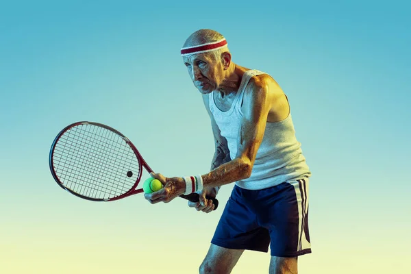 Starszy mężczyzna gra w tenisa w sporcie na gradientowym tle i neonowym świetle — Zdjęcie stockowe