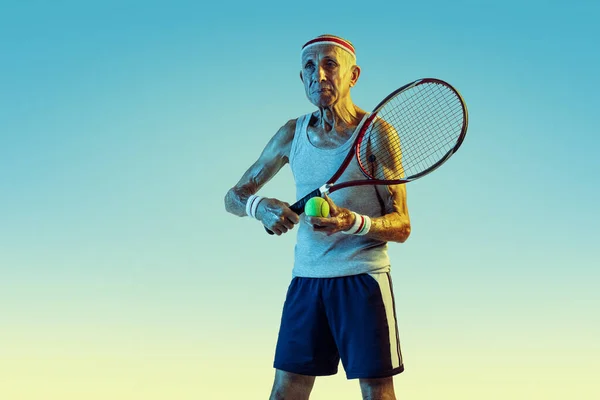 Senior-Mann spielt Tennis in Sportbekleidung auf Steigungsuntergrund und Neonlicht — Stockfoto
