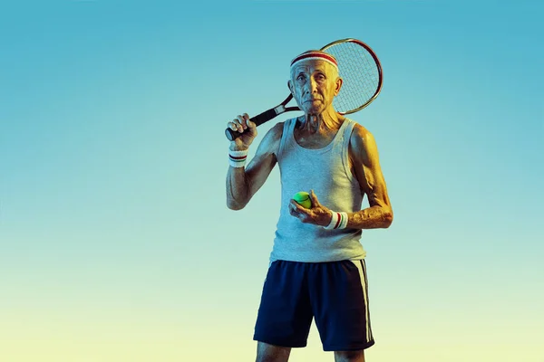 Homem sênior jogando tênis em sportwear no fundo gradiente e luz de néon — Fotografia de Stock