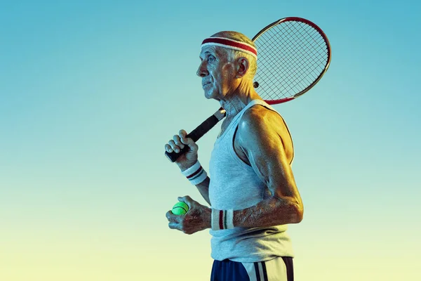 Uomo anziano che gioca a tennis in abbigliamento sportivo su sfondo sfumato e luce al neon — Foto Stock