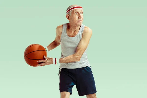 Senior man playing basketball in sportwear isolated on green background