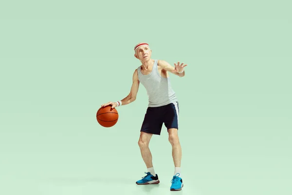 Senior man playing basketball in sportwear isolated on green background