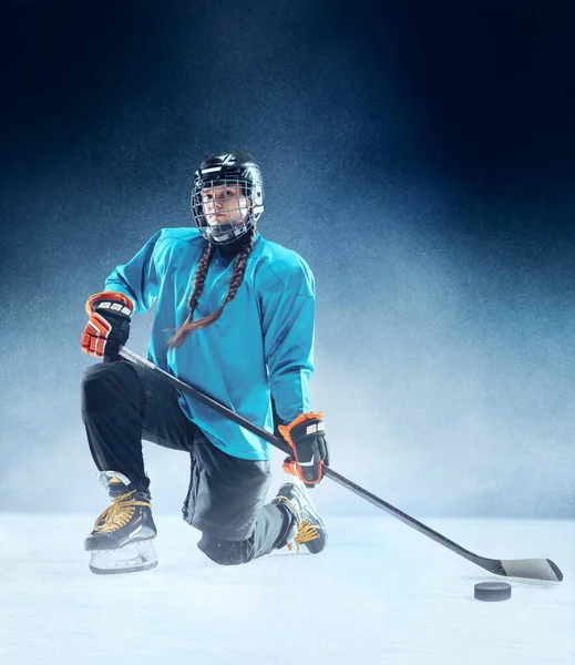 Junge Hockeyspielerin mit Stock auf dem Eis und blauem Hintergrund — Stockfoto