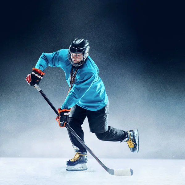 Joven jugadora de hockey con el palo en la pista de hielo y fondo azul —  Fotos de Stock