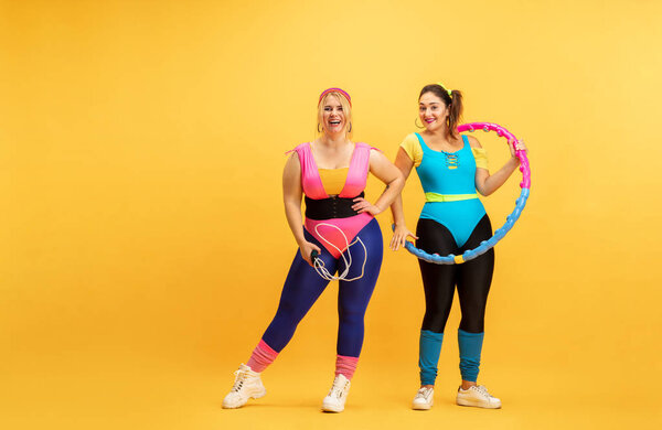 Young caucasian plus size female models training on yellow background