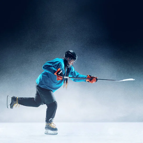 Fiatal női hoki játékos a bottal a jégpályán és a kék háttér — Stock Fotó