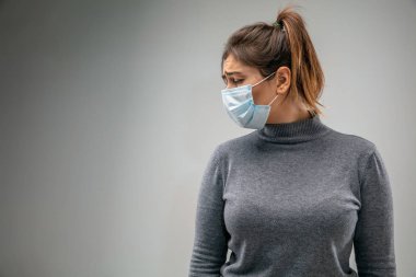 Solunum maskesi takan beyaz kadın hava kirliliğine karşı ve gri stüdyo arka planında alacakaranlığa karşı
