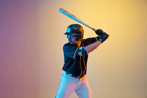 Jogador de beisebol, arremessador de uniforme preto praticando em fundo gradiente em luz de néon — Fotografia de Stock