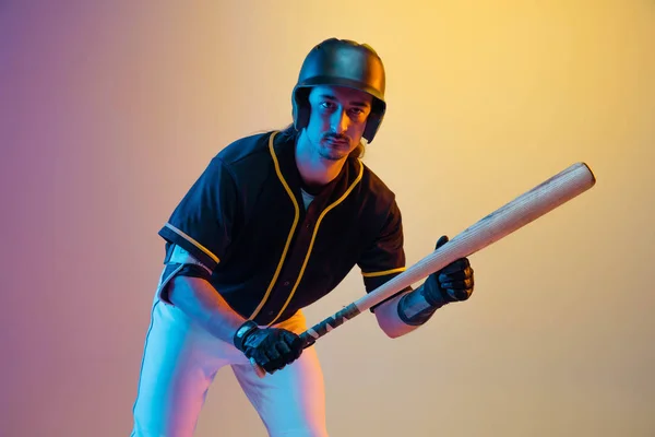 Jogador de beisebol, arremessador de uniforme preto praticando em fundo gradiente em luz de néon — Fotografia de Stock