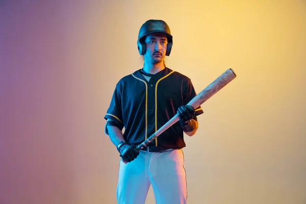 Jogador de beisebol, arremessador de uniforme preto praticando em fundo gradiente em luz de néon — Fotografia de Stock