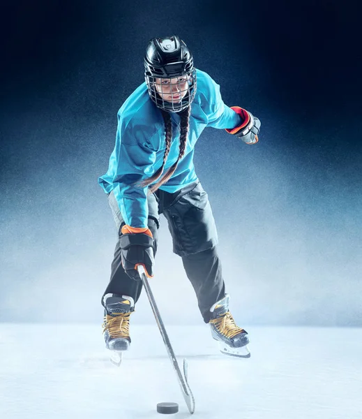 Young female hockey player with the stick on ice court and blue background — Stock Photo, Image