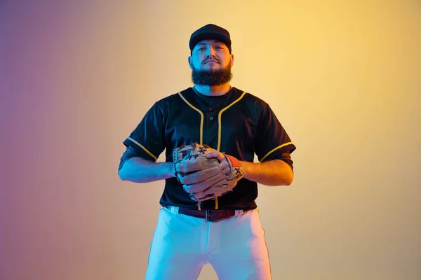 Baseball player, pitcher in a black uniform practicing on gradient background in neon light