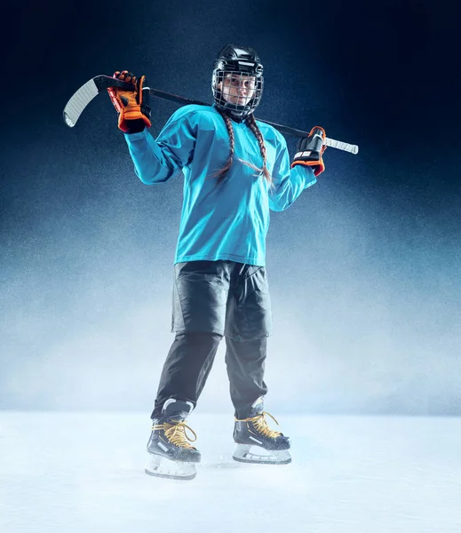 Joven jugadora de hockey con el palo en la pista de hielo y fondo azul — Foto de Stock