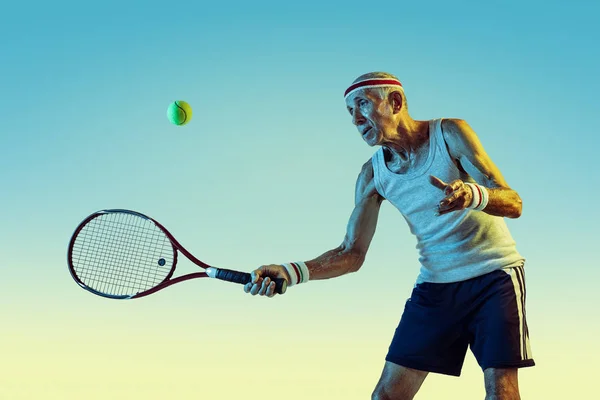 Homem sênior jogando tênis em sportwear no fundo gradiente e luz de néon — Fotografia de Stock