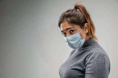 Solunum maskesi takan beyaz kadın hava kirliliğine karşı ve gri stüdyo arka planında alacakaranlığa karşı