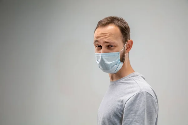 Solunum maskesi takan beyaz bir adam hava kirliliğine karşı ve gri stüdyo arka planında alacakaranlığa karşı — Stok fotoğraf