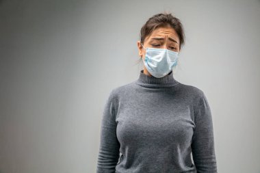 Solunum maskesi takan beyaz kadın hava kirliliğine karşı ve gri stüdyo arka planında alacakaranlığa karşı