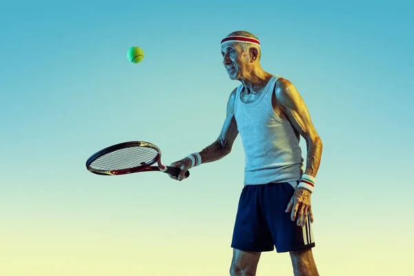 Старший мужчина играет в теннис в спортивной форме на градиентном фоне и неоновом свете — стоковое фото