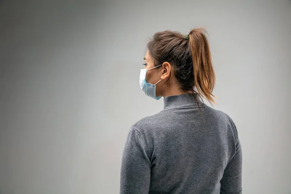 Mujer caucásica que usa la máscara de protección respiratoria contra la contaminación del aire y el atardecer en el fondo gris del estudio — Foto de Stock