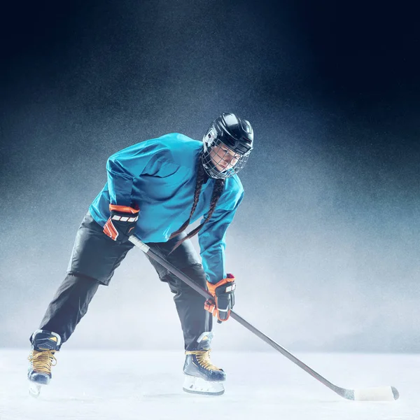 Joven jugadora de hockey con el palo en la pista de hielo y fondo azul — Foto de Stock