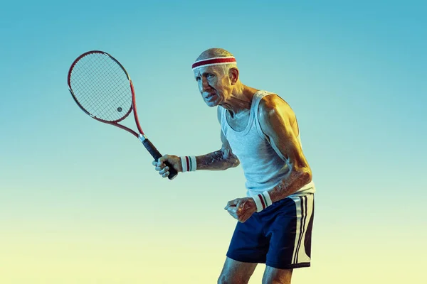 Homem sênior jogando tênis em sportwear no fundo gradiente e luz de néon — Fotografia de Stock