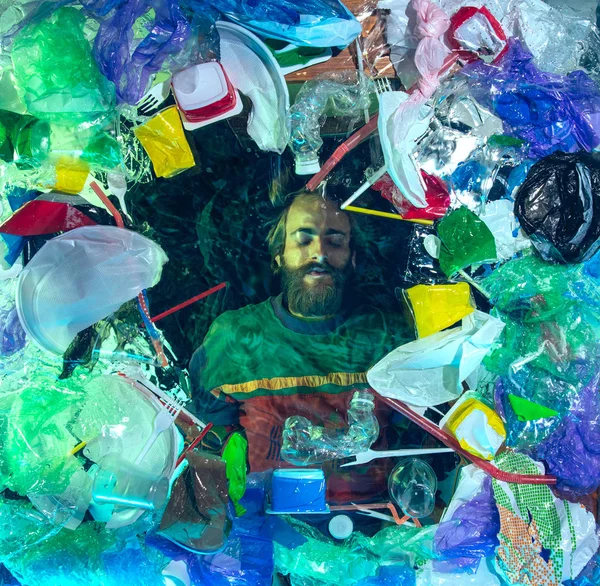 Man drowning in ocean water under plastic recipients pile, environment concept