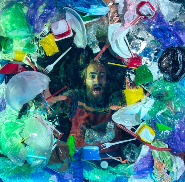 Man drowning in ocean water under plastic recipients pile, environment concept