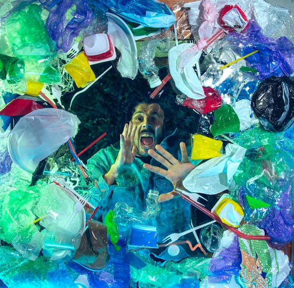 Man drowning in ocean water under plastic recipients pile, environment concept