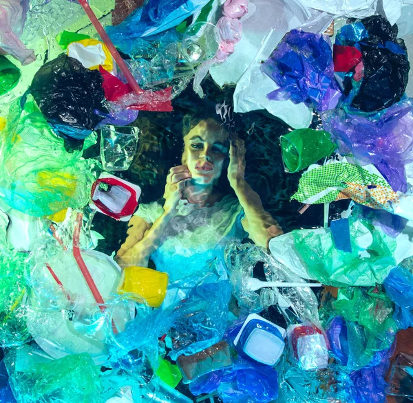 Woman drowning in ocean water under plastic recipients pile, environment concept