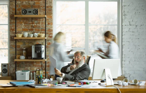 Nervioso y cansado jefe en su lugar de trabajo ocupado mientras la gente que se mueve cerca borrosa — Foto de Stock