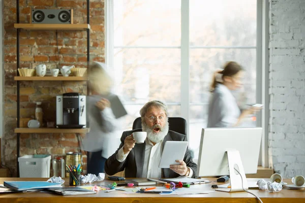 Nervioso y cansado jefe en su lugar de trabajo ocupado mientras la gente que se mueve cerca borrosa — Foto de Stock