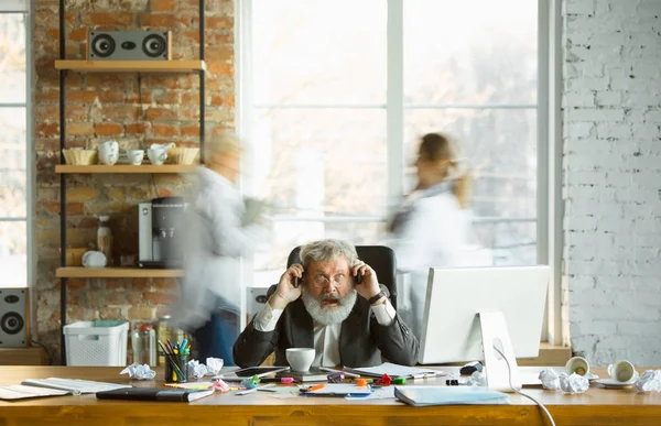 Nervózní a unavený šéf na svém pracovišti, zatímco lidé pohybující se v blízkosti rozmazané — Stock fotografie